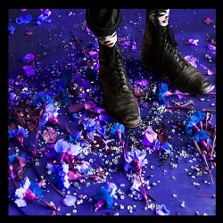 SHAKEY GRAVES – Kids These Days; zwei Füße in Lederstiefeln, die auf zerrupften Blüten stehen