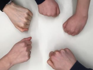 Fünf Hände die auf einen weißen Tisch klopfen.