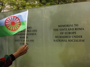 Hand mit Flagge vor Gedenktafel